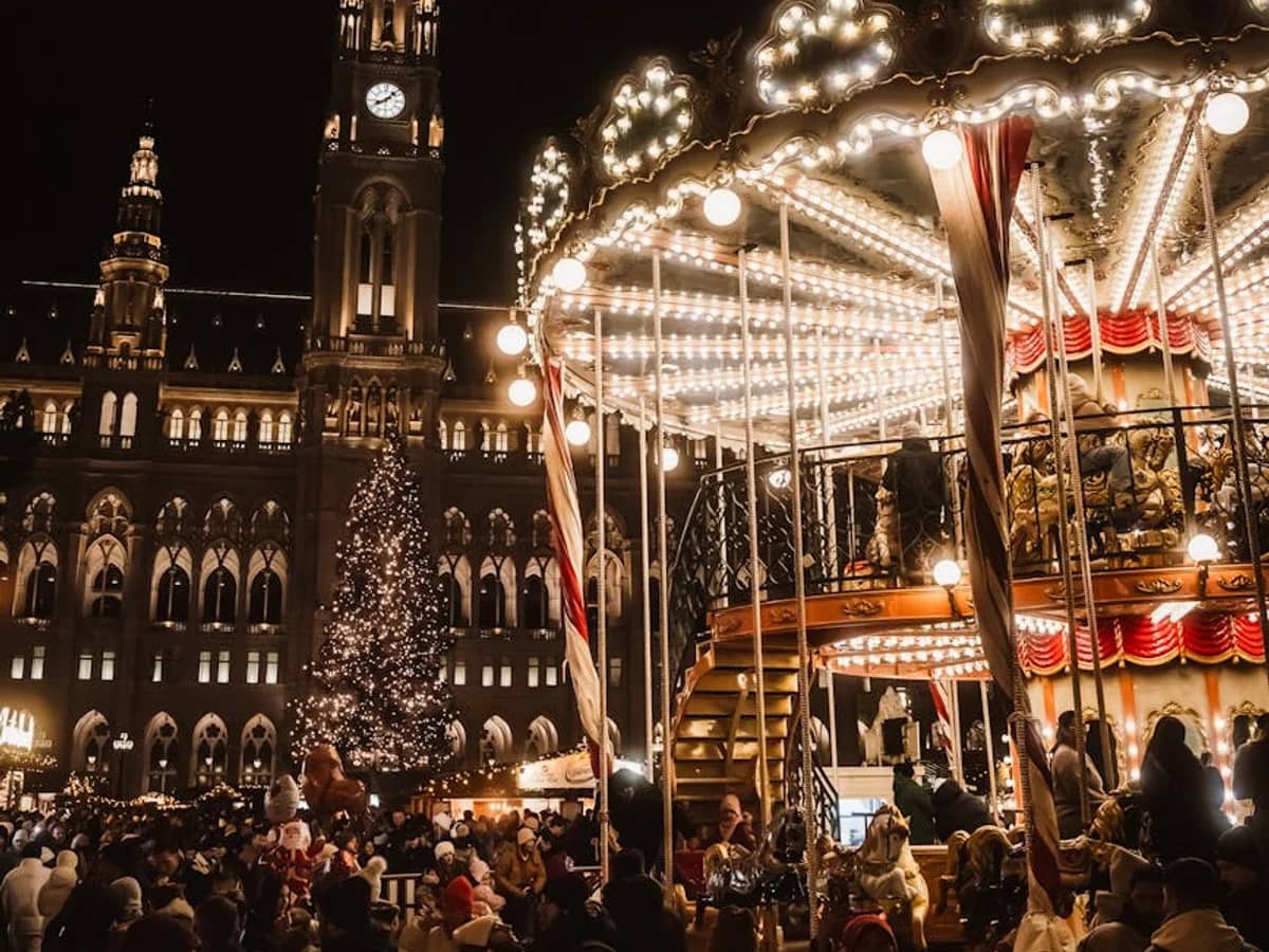Vienna Rathaus illuminated at Christmas behind a traditional carousel