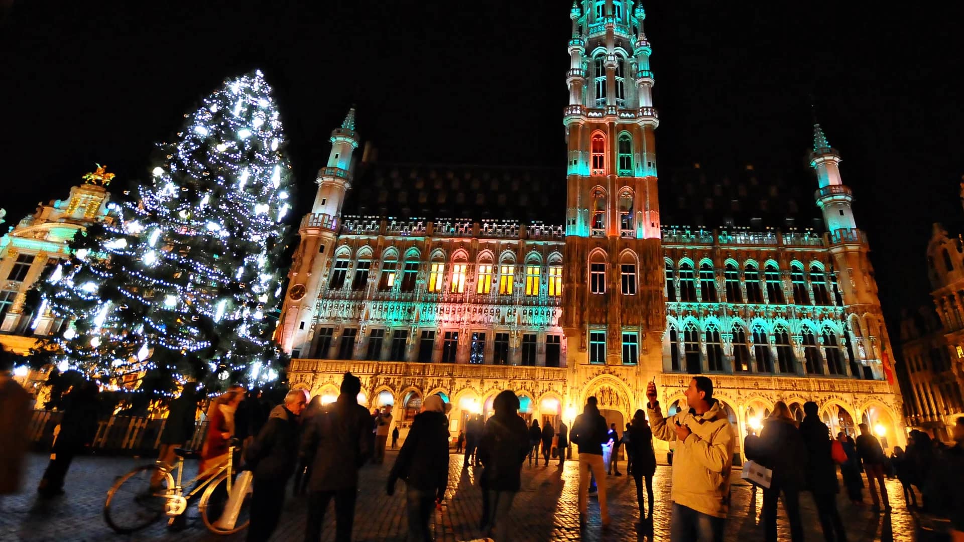Brussels Grand Place illuminated for Christmas with festive lights and a glowing tree.