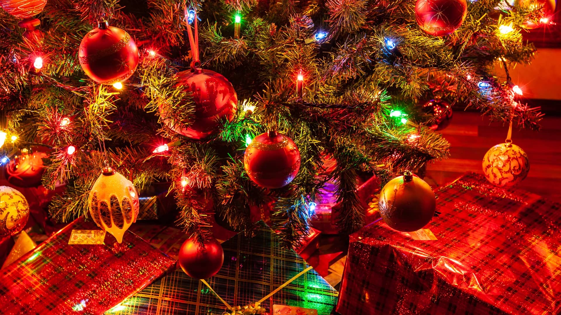 Festive Christmas tree adorned with decorations and presents under twinkling market lights.