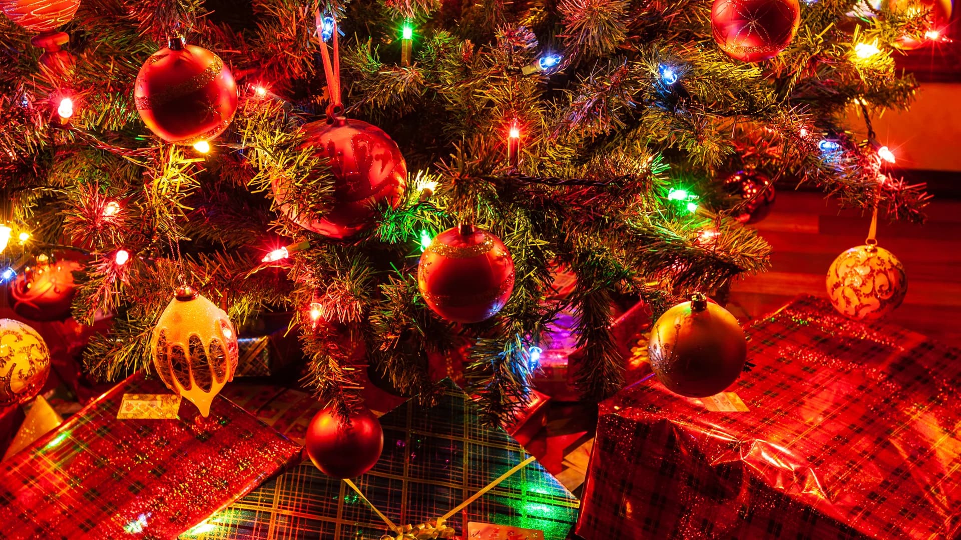 Festive Christmas tree adorned with decorations and presents under twinkling market lights.