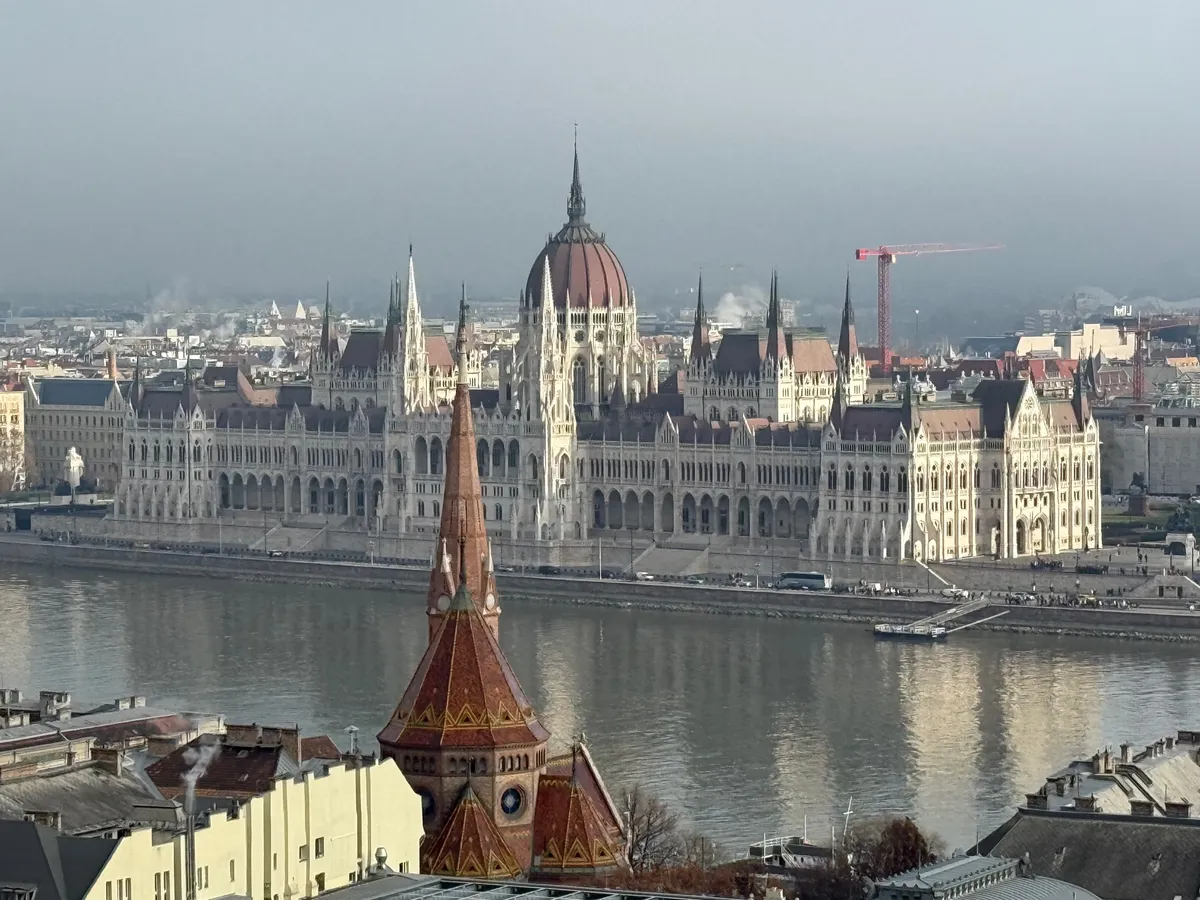 Aerial view of Budapest's Parliament Building under an overcast sky, showcasing an unknown festive atmosphere with no visible Christmas market decorations.