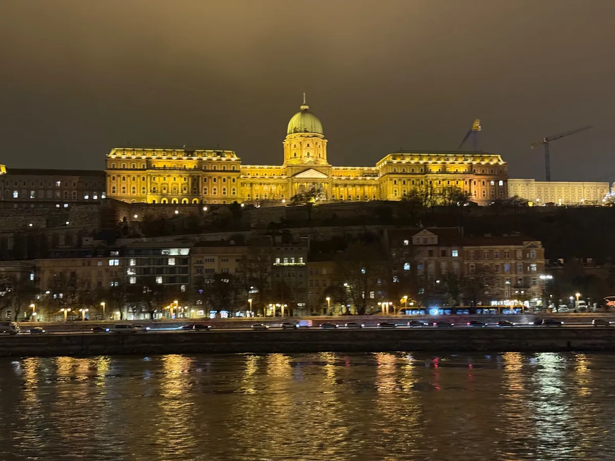 Illuminated government building reflecting in river at dusk with festive decorations and lights near Unknown Christmas market.