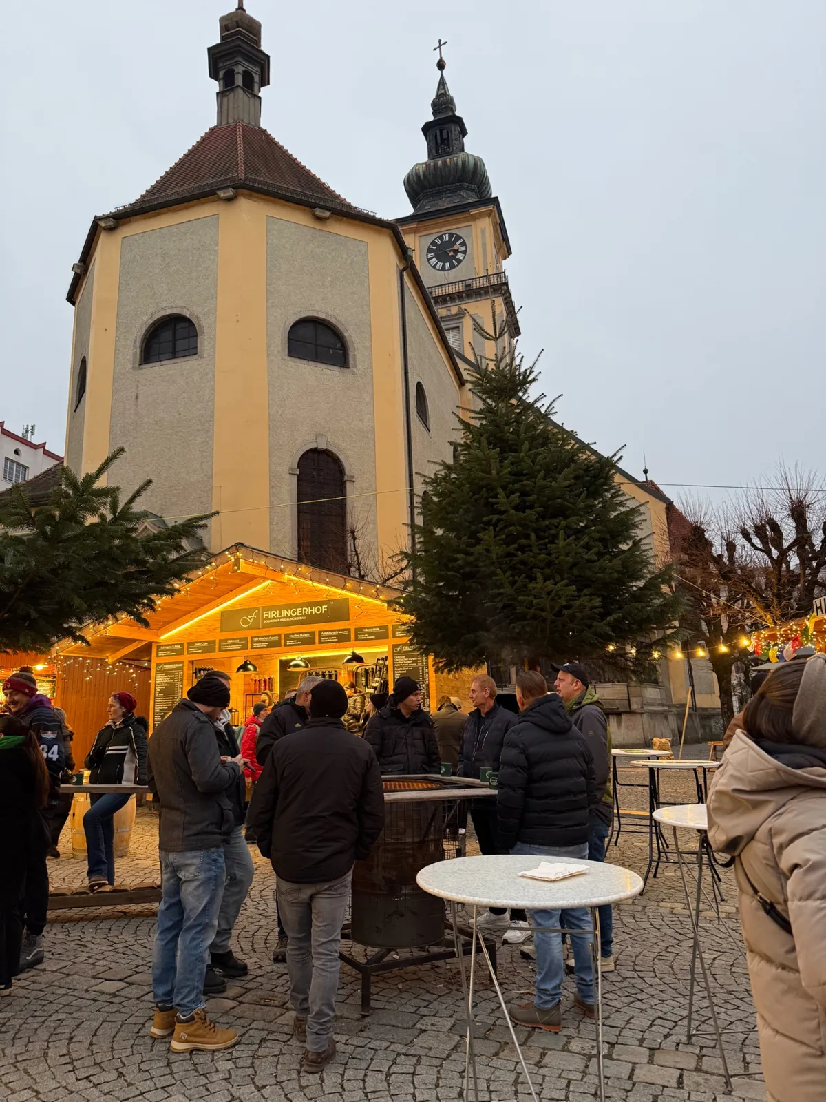 Festive atmosphere at an Unknown Christmas market with decorations and lights near a charming yellow church.