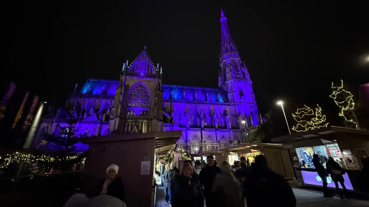 Festive decorations and lights illuminate the Unknown Christmas market beneath a Gothic cathedral.