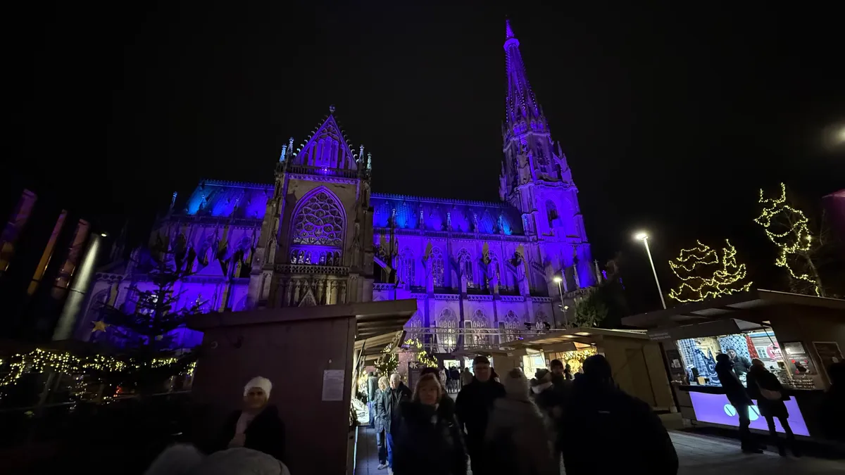 Festive decorations and lights illuminate the Unknown Christmas market beneath a Gothic cathedral.