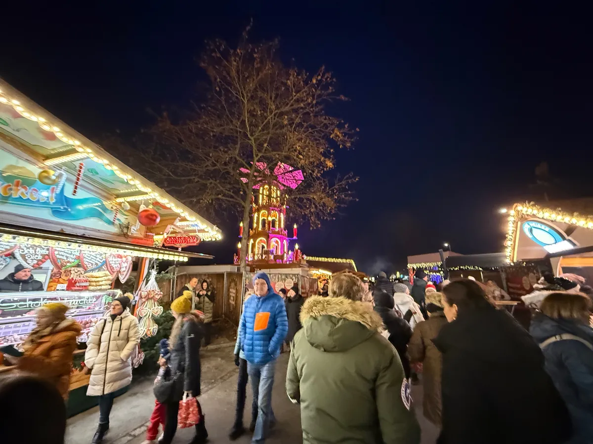 Festive decorations and lights illuminate a lively Unknown Christmas market scene under a dark blue sky.