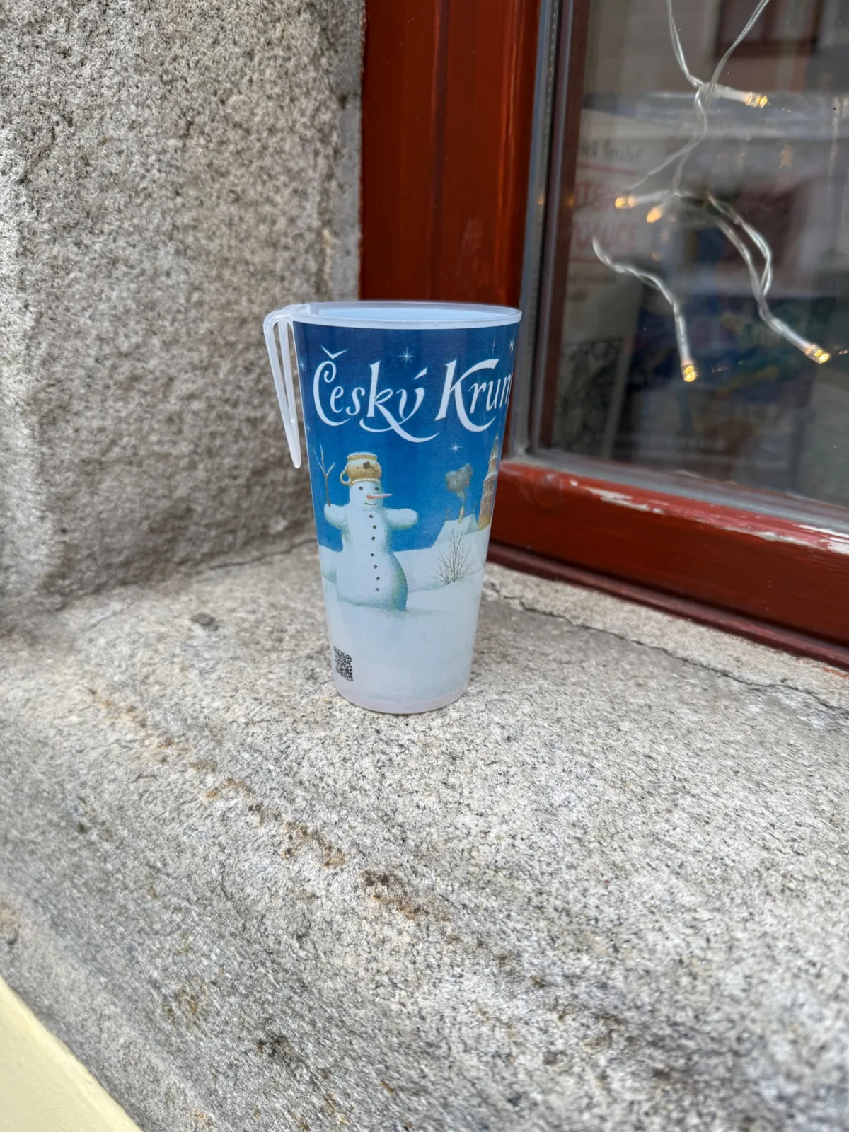 Festive decorations and lights at an Unknown Czech Christmas market with a snowman cup.