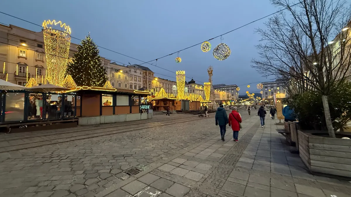 Unknown Christmas market at twilight with festive decorations and warm lights glowing under a serene blue sky.