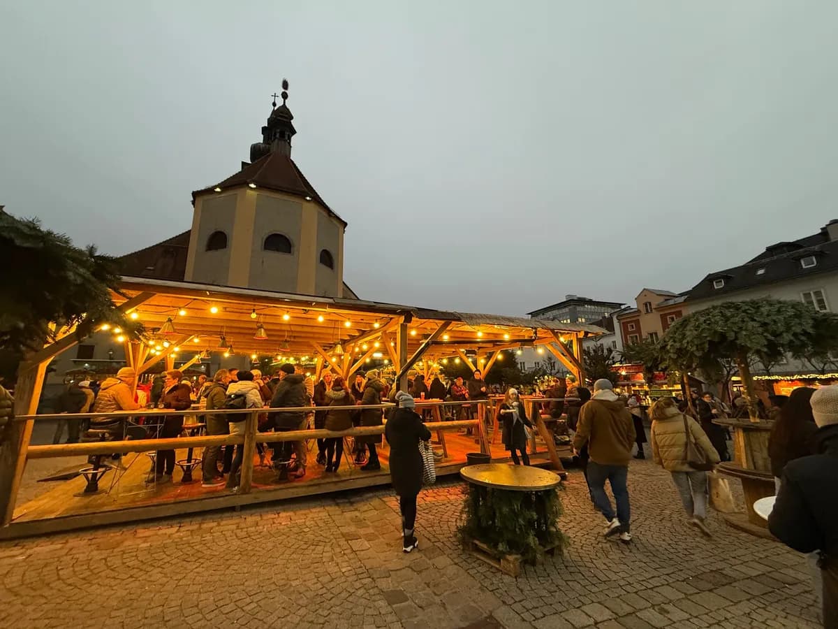 Festive decorations and warm lights illuminate an Unknown Christmas market under a historic church tower.