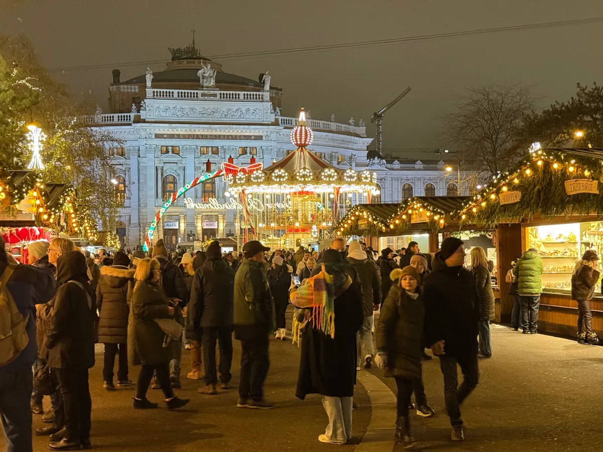 Vibrant Unknown Christmas market with festive decorations and lights, featuring a carousel and the historic Burgtheater in Vienna.