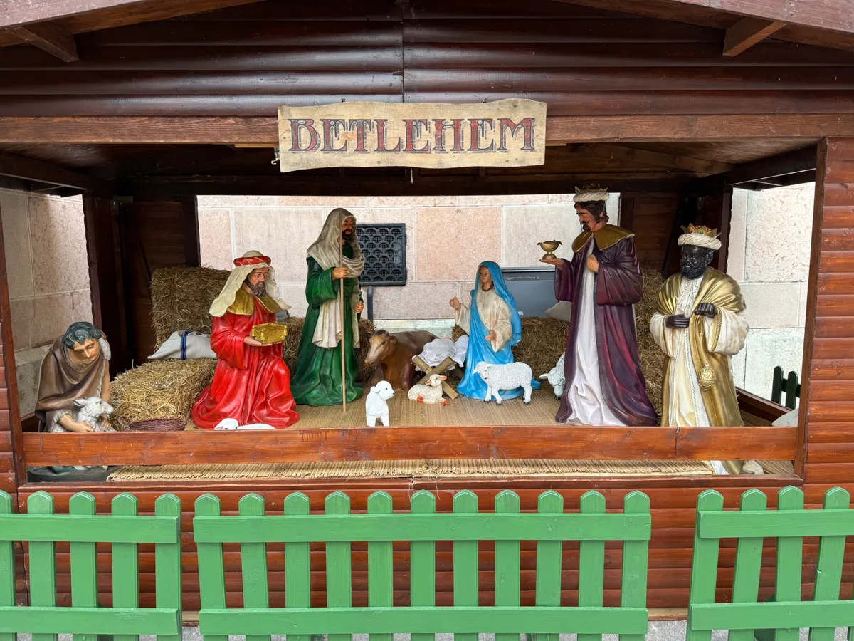 Unknown festive nativity scene with decorations at a German Christmas market, showcasing lights and traditional figures.