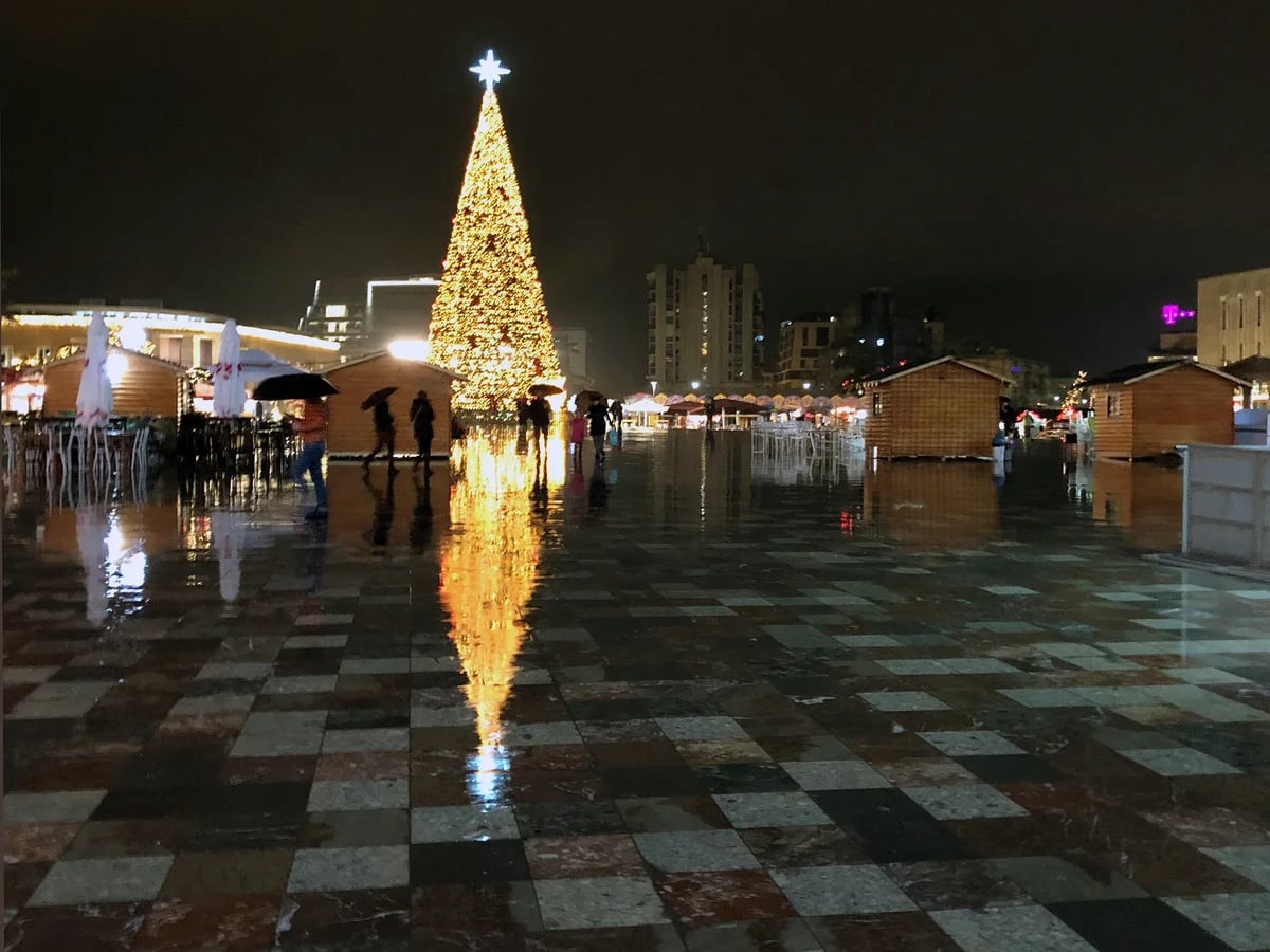 Joulutori illuminated Christmas tree in Tampere's Central Square reflecting on wet pavement, festive atmosphere with stalls and cathedral