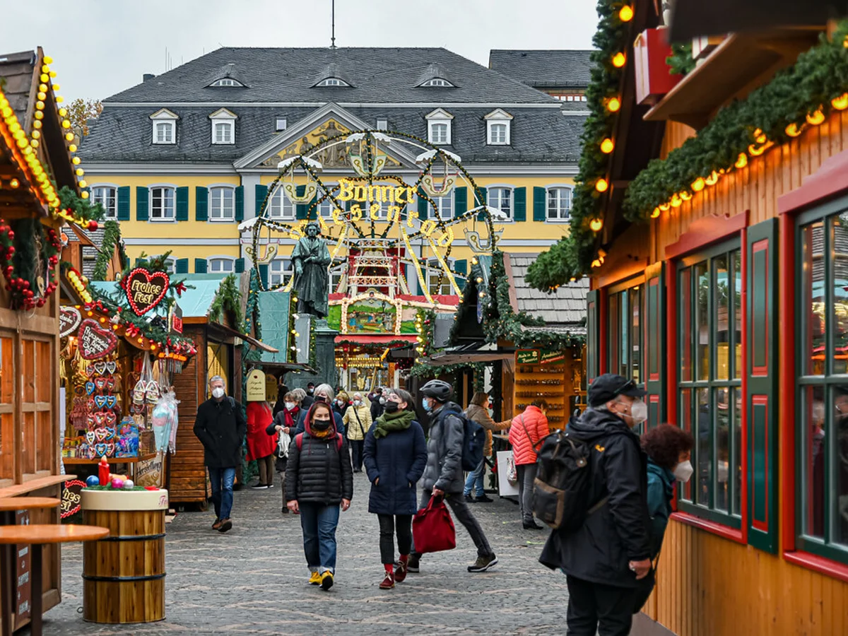 Bonner Weihnachtsmarkt - Münsterplatz bustling with visitors in Bonn, showcasing festive stalls beneath the Kurfürstliches Schloss