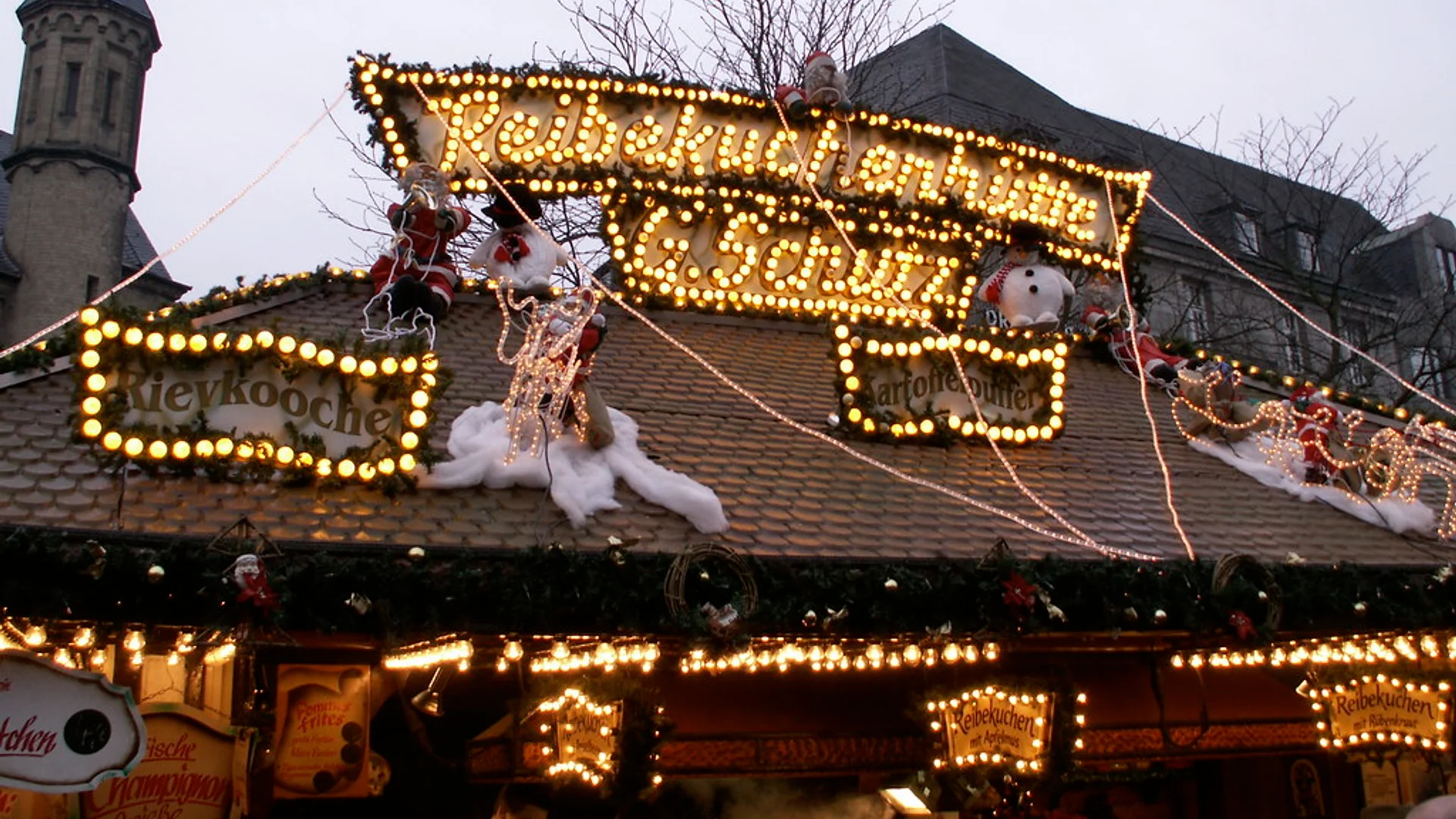 Bonner Weihnachtsmarkt stall glowing warmly in Bonn at twilight with St. Remigius Church spire in view