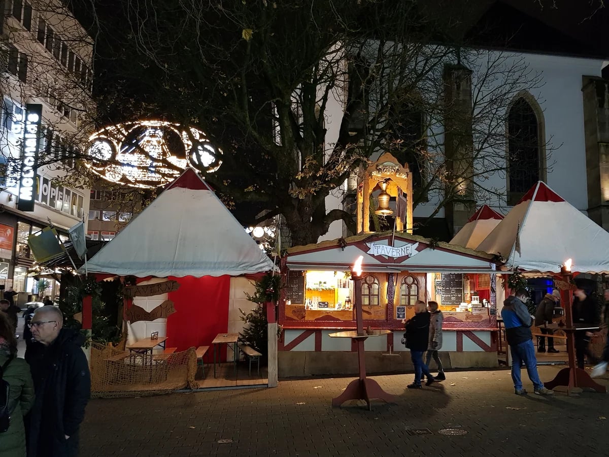 Mittelaltermarkt Essen medieval stalls glowing warmly against twilight sky with Essen Münster cathedral