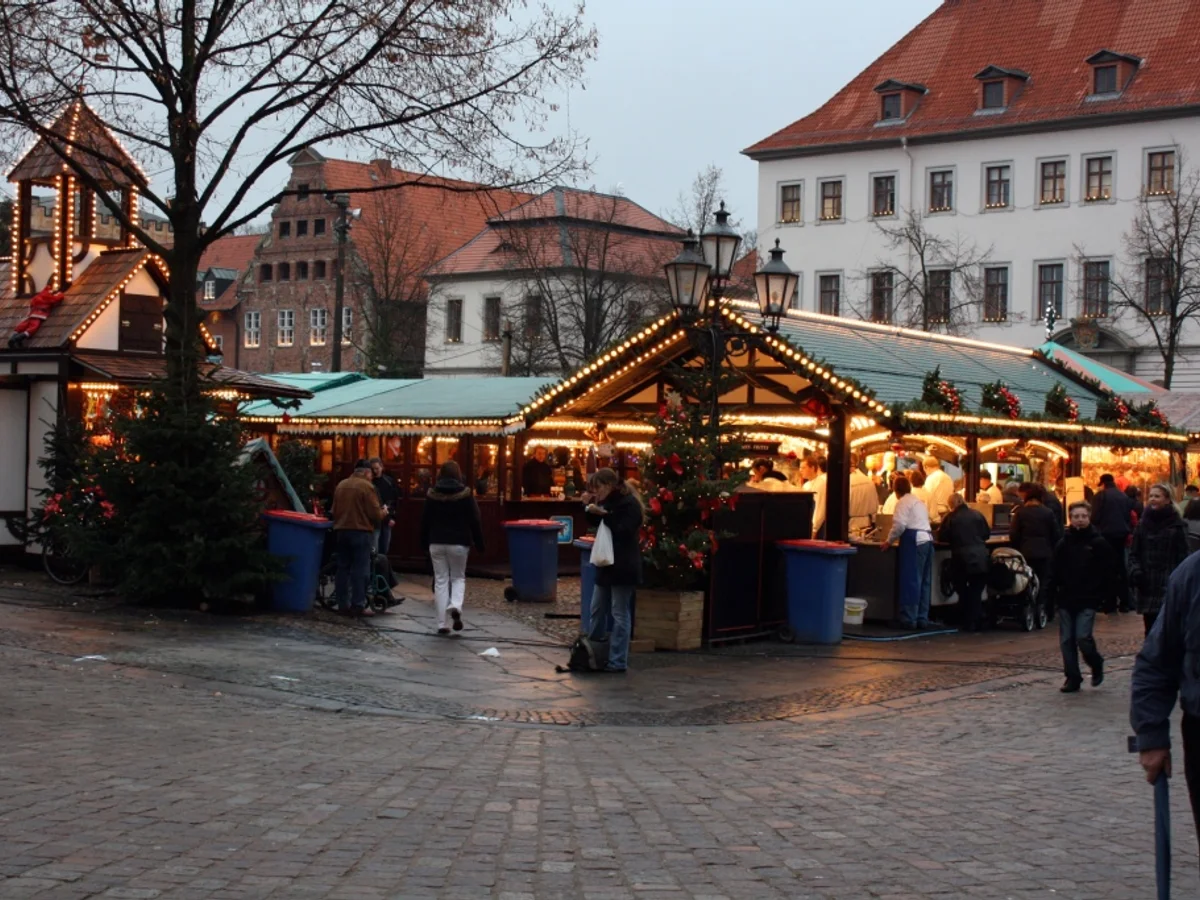 TO HUUS Weihnachtsmarkt warm lights illuminate market stalls in Lüneburg twilight, historic architecture backdrop