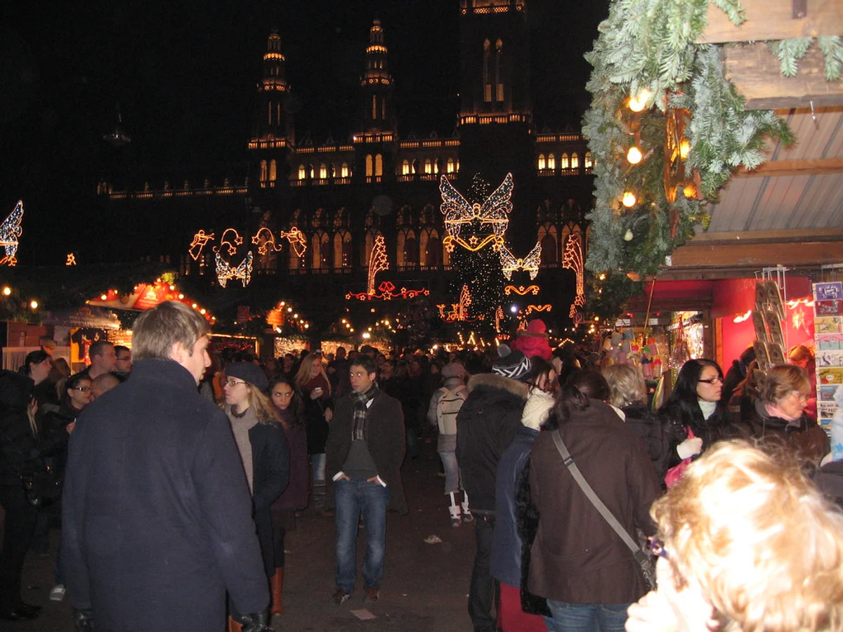 Christkindlmarkt - Neupfarrplatz bustling crowds in Regensburg under St. Peter's Cathedral's illuminated spires.