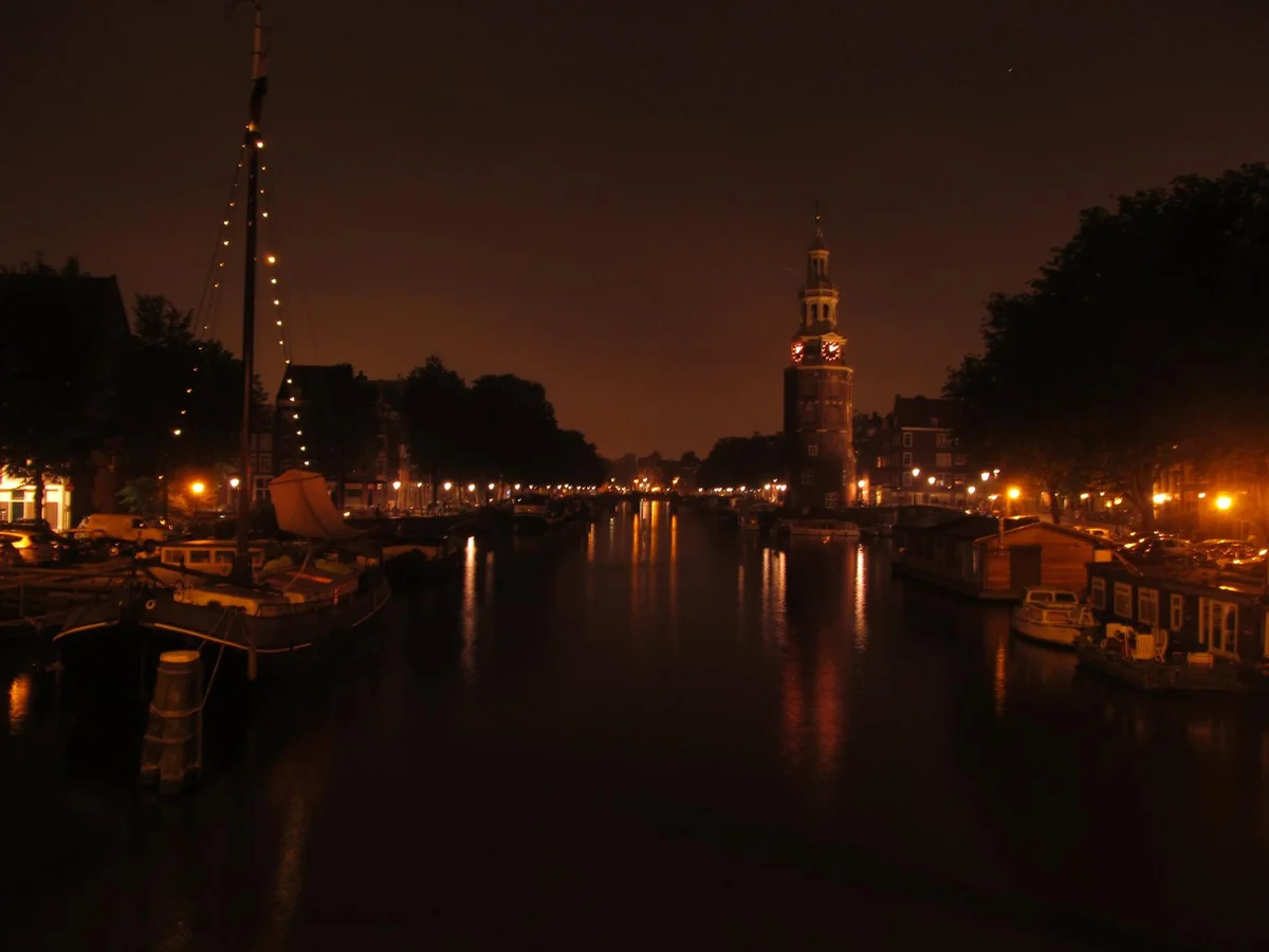 Amsterdam canal scene at dusk with Montelbaanstoren tower reflecting in water