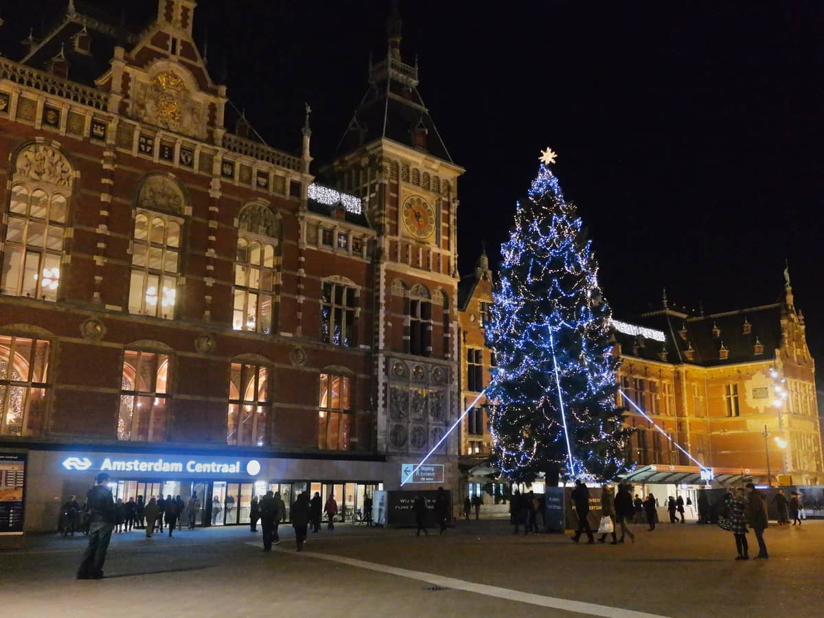 Amsterdam Central Station frames a stunning blue-lit Christmas tree during winter festivities.